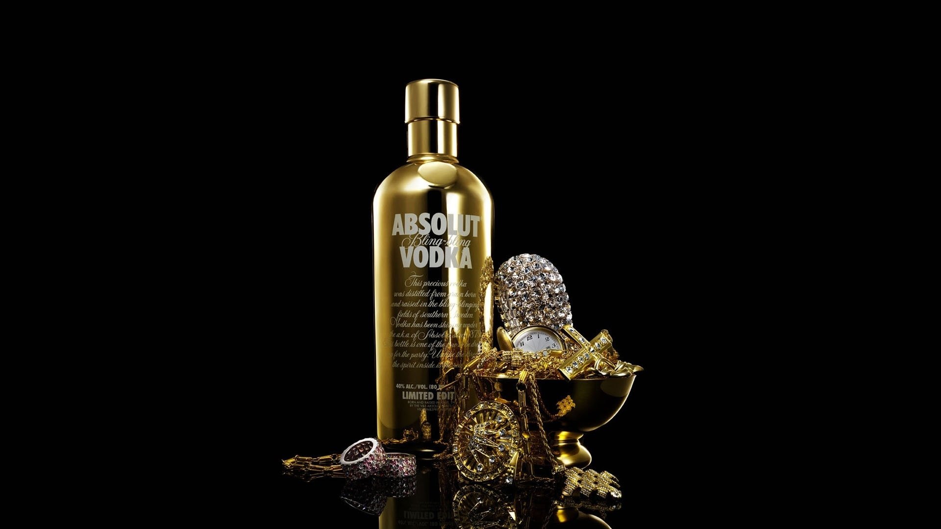A man-made, gold Absolut Vodka bottle surrounded by sparkling jewelry and accessories on a reflective black surface.