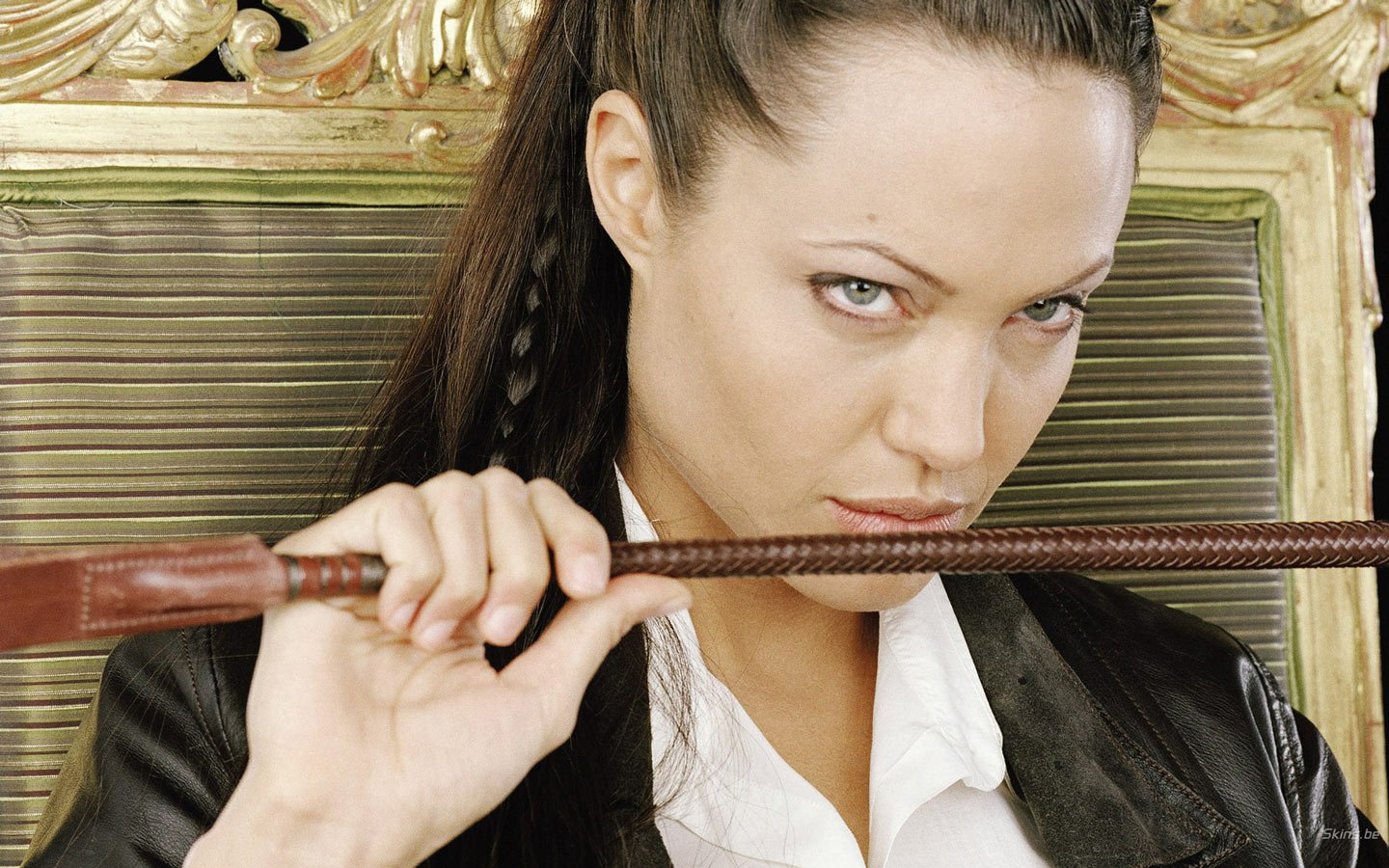 Angelina Jolie poses confidently with a whip, seated on an ornate throne, exuding a fierce and captivating presence in this striking portrayal.