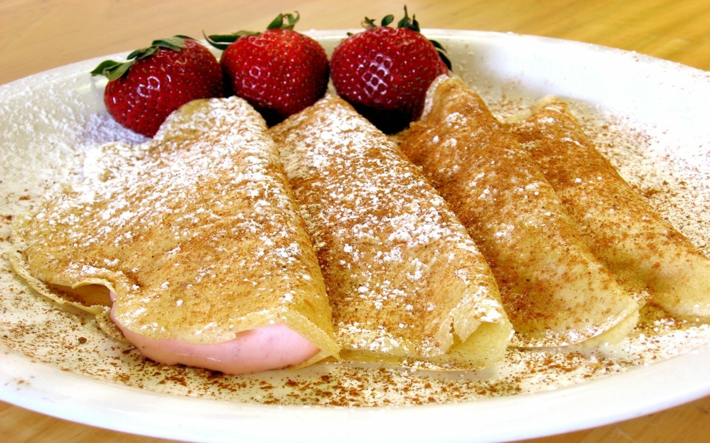 A plate of delicious crêpes dusted with powdered sugar, served with fresh strawberries on the side, creating an enticing dessert presentation.