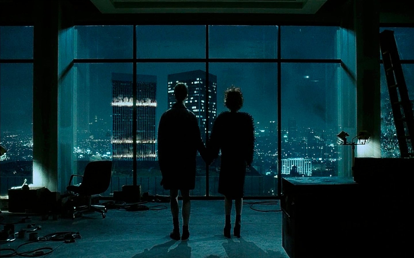 A silhouetted couple stands hand in hand, gazing out at a city skyline through a large window in a dimly lit room, capturing a poignant moment reminiscent of *Fight Club*.