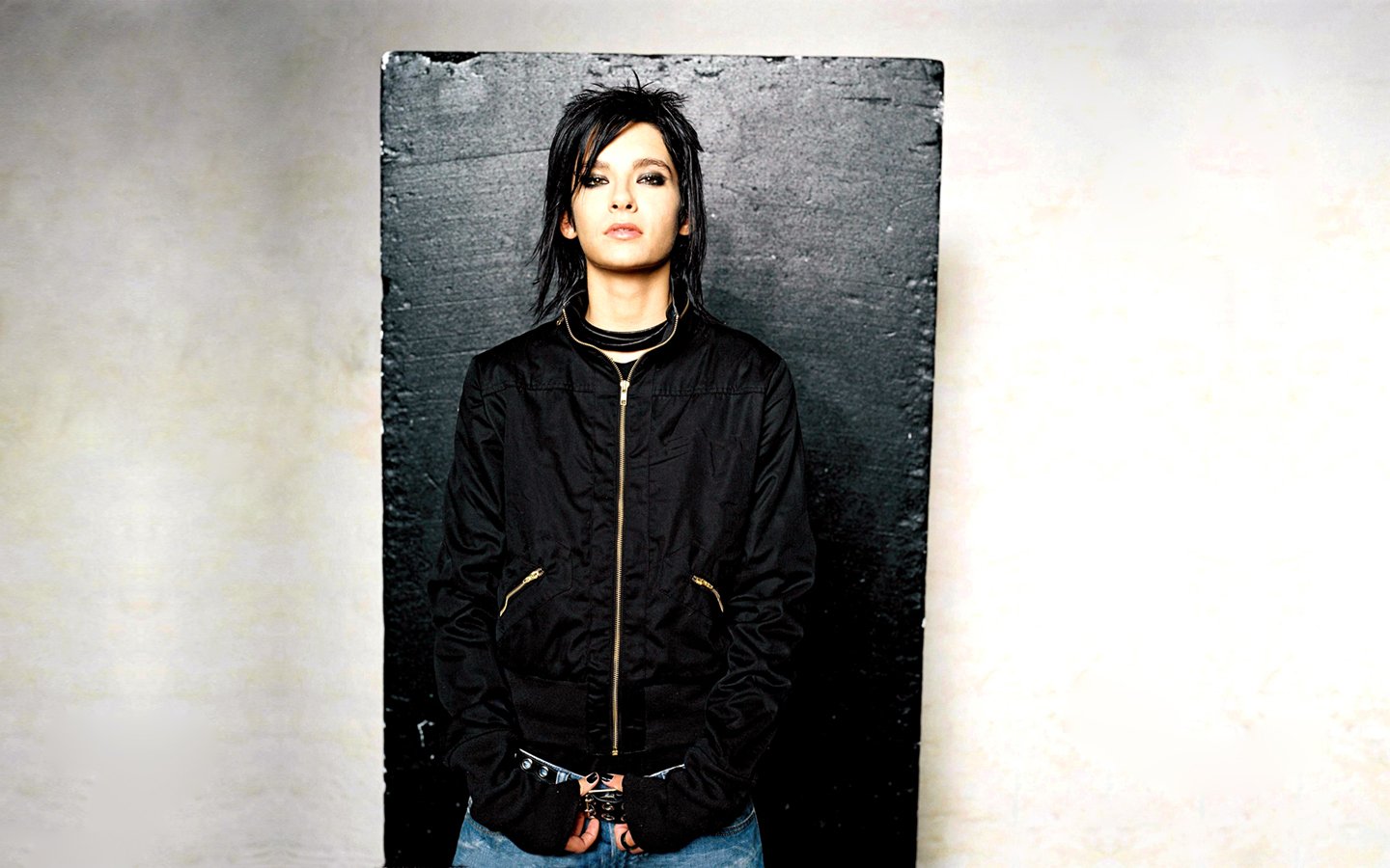Portrait of a member of Tokio Hotel standing against a textured black and white wall, embodying the band's edgy music style.
