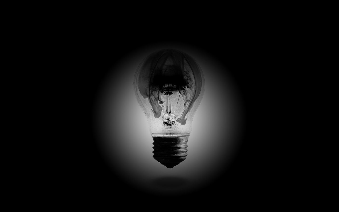 A glowing man-made light bulb illuminates against a dark background, highlighting its intricate filament inside.