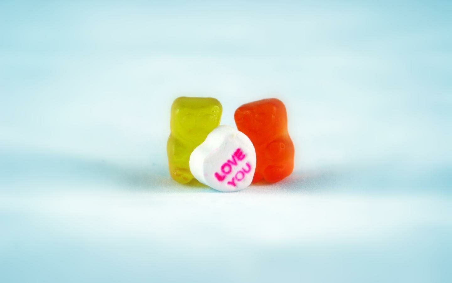 A colorful assortment of gummy candies, including two bear-shaped pieces and a heart-shaped candy, with the text LOVE YOU printed prominently on the white candy.