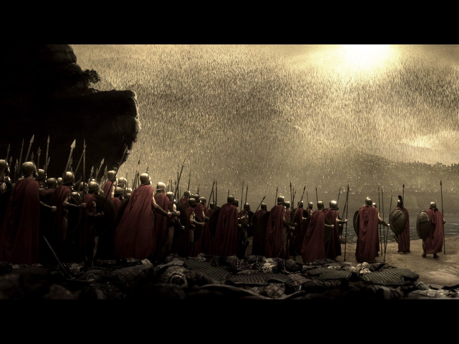 A dramatic scene from the movie 300, featuring Spartan warriors in armor and red cloaks, standing resolutely against a backdrop of rain and a moody sky.