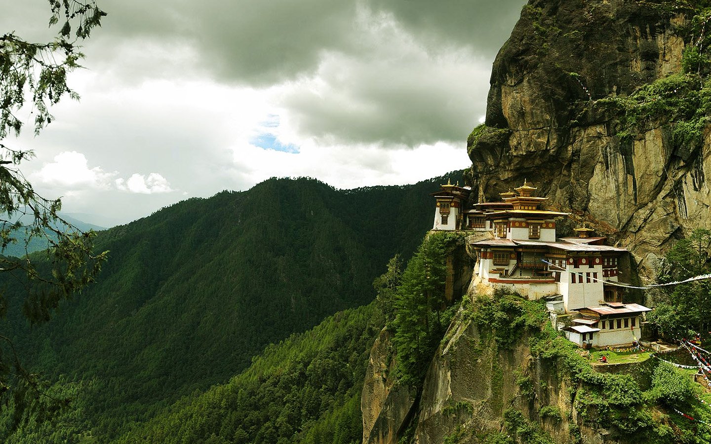A stunning view of Paro Taktsang, a religious monastery perched high on a cliff, surrounded by lush mountains and cloudy skies.