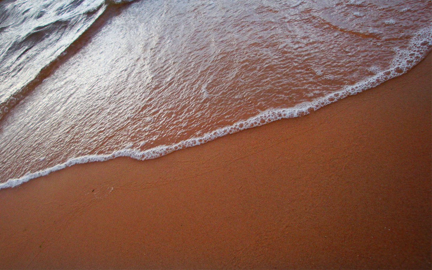 Gentle waves lap against a sandy beach, showcasing the serene beauty of nature. The water glistens as it meets the shore, creating a tranquil coastal scene.