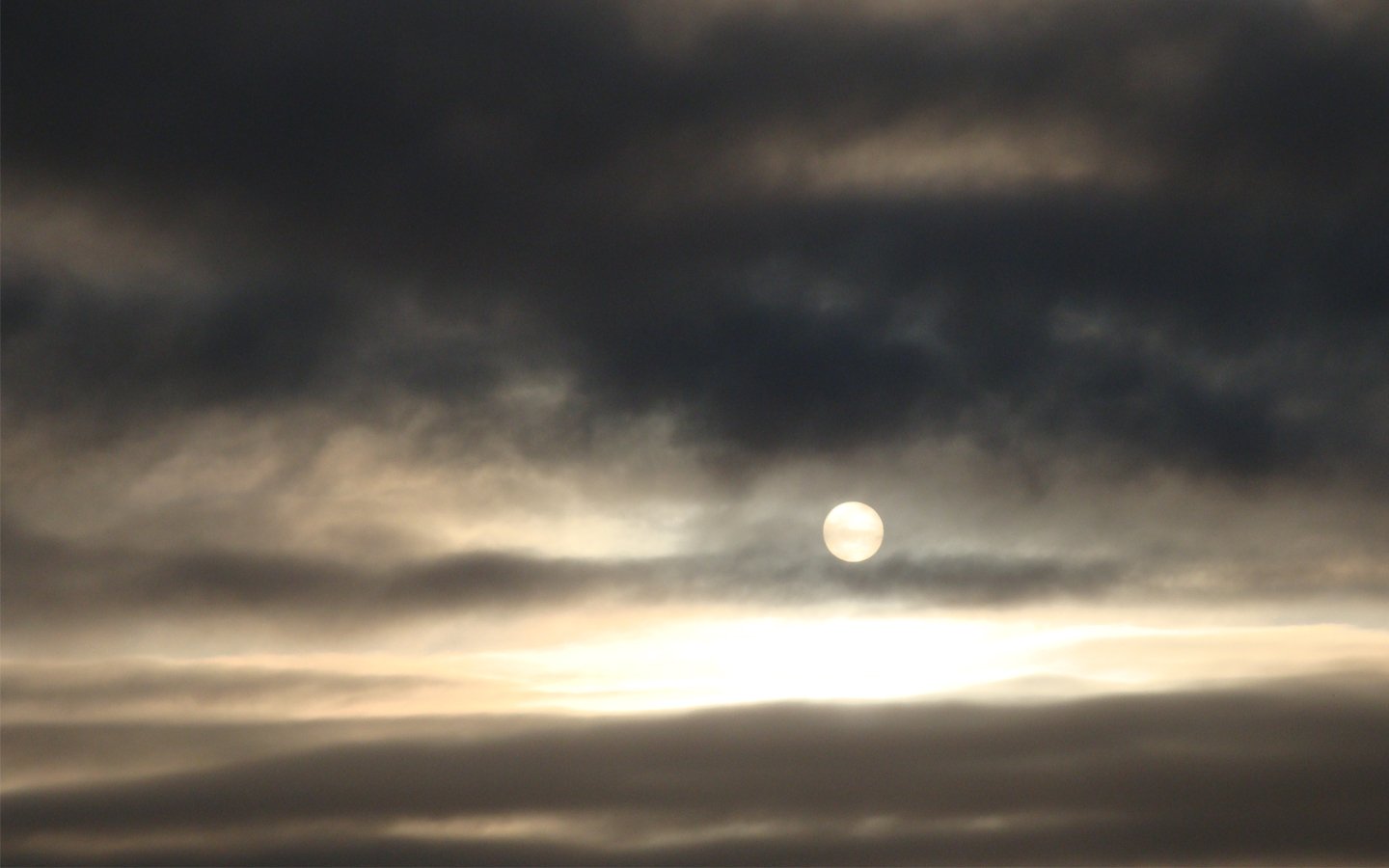 A serene landscape showcasing the sun peeking through a dramatic layer of clouds, capturing the beauty of nature in a captivating interplay of light and shadow.