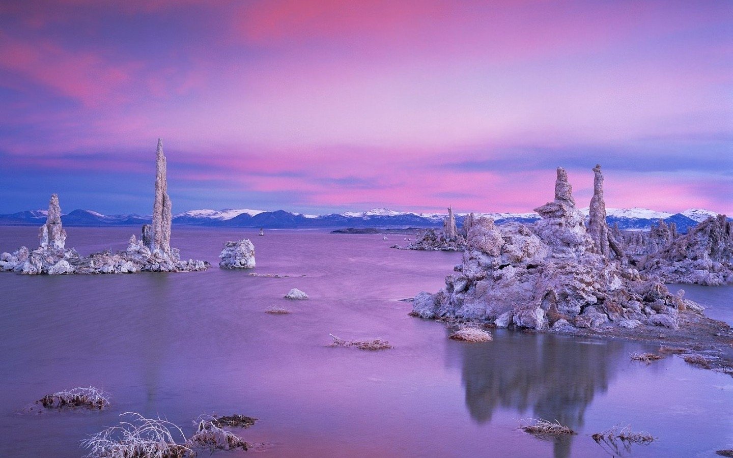 A serene lake scene at dusk, featuring striking rock formations and reflections in the water, with a dramatic sky painted in shades of pink and purple.