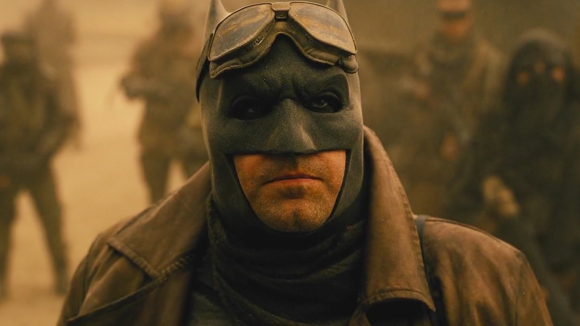 Grim Batman wearing goggles and a worn cowl in a dusty battlefield — scene from the movie Batman V Superman: Dawn Of Justice.