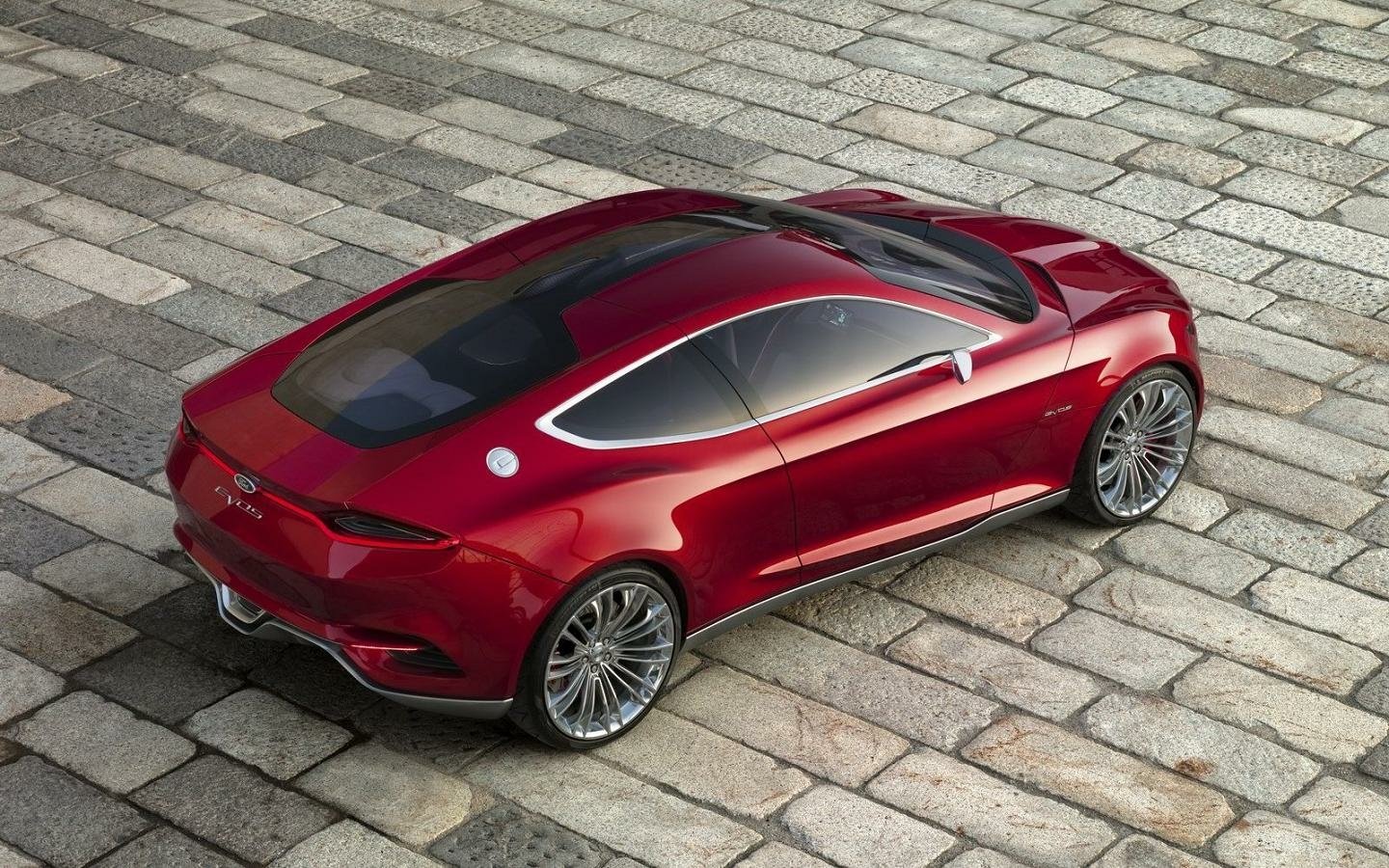Red Ford Evos vehicle seen from a high rear three-quarter angle on cobblestone, highlighting sleek coupe lines, large alloy wheels and a panoramic glass roof.