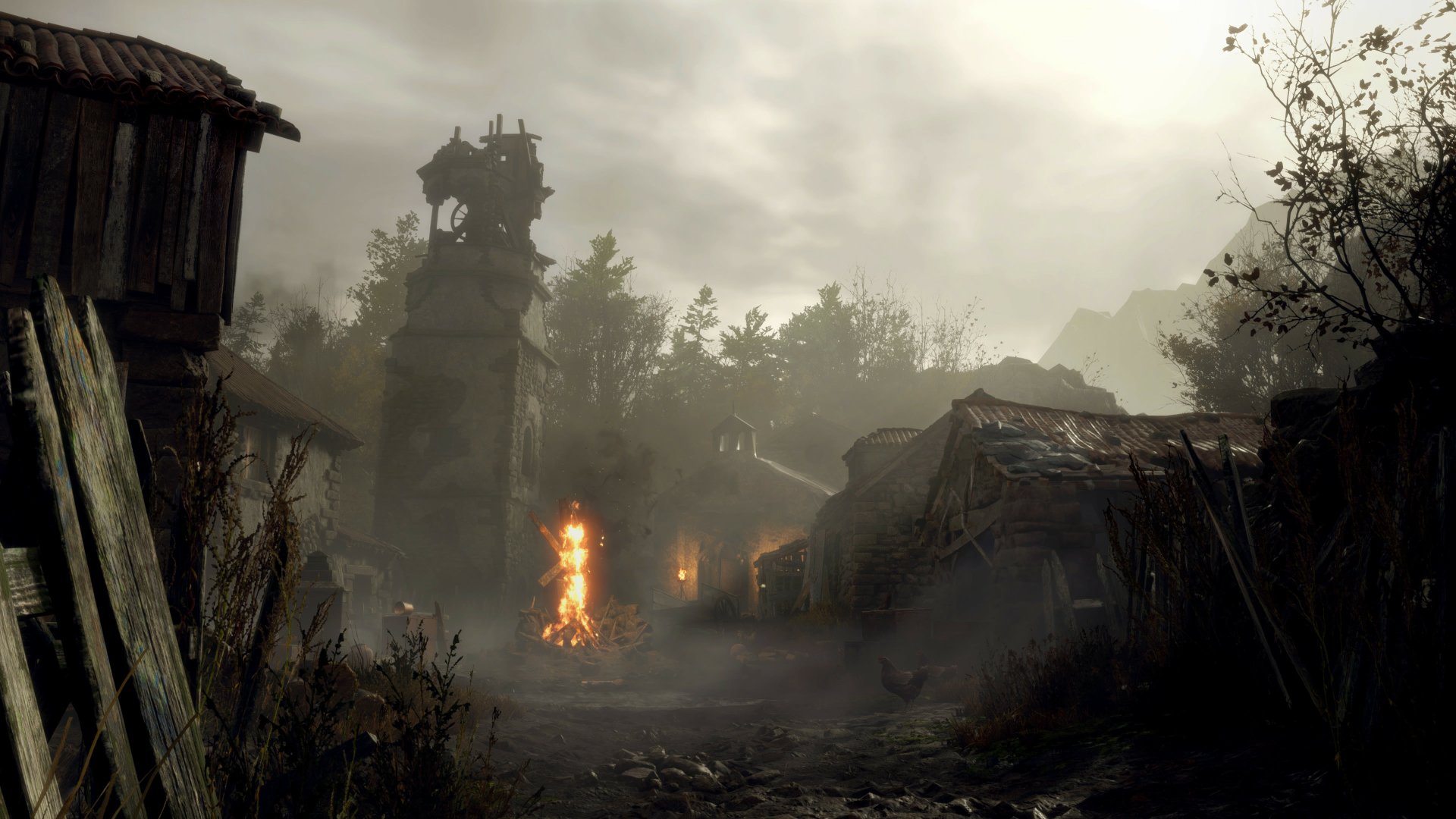 Fog-shrouded rural village with ruined huts and a burning effigy beneath a stormy sky — scene from Resident Evil 4 (2023).