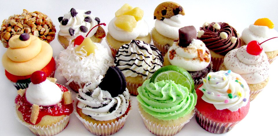 Assorted cupcakes with colorful frosting and varied toppings — sprinkles, chocolate, fruit and nuts — a display of sweet dessert treats.
