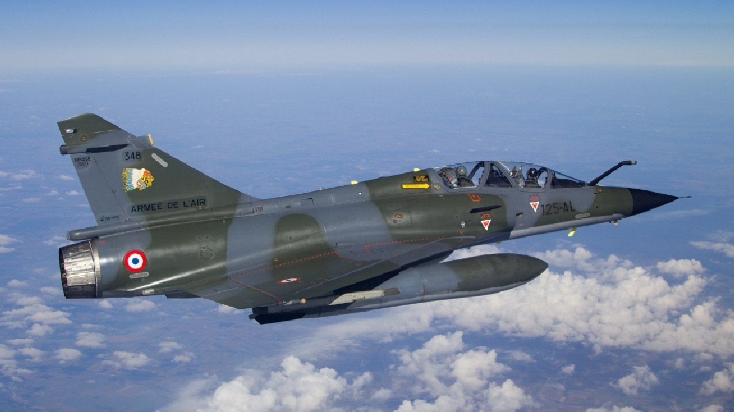 Military Dassault Mirage 2000 fighter jet in flight above a layer of clouds against a clear blue sky.