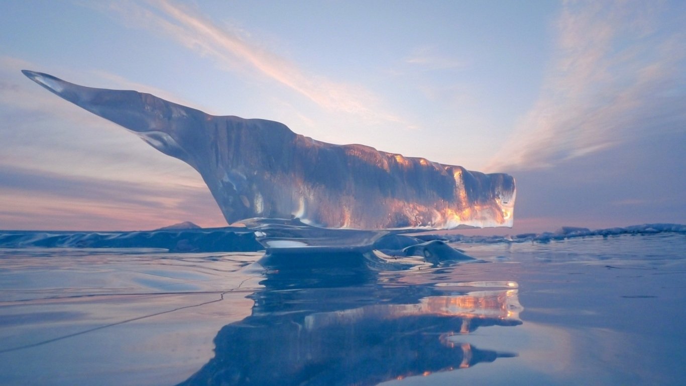 A large, translucent iceberg rests on icy water under a soft, pastel sky, capturing the serene beauty of nature in a cold, remote landscape.
