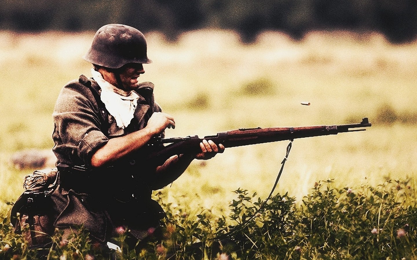 Military soldier kneeling in a grassy field, wearing a helmet and uniform while loading or aiming a bolt-action rifle.