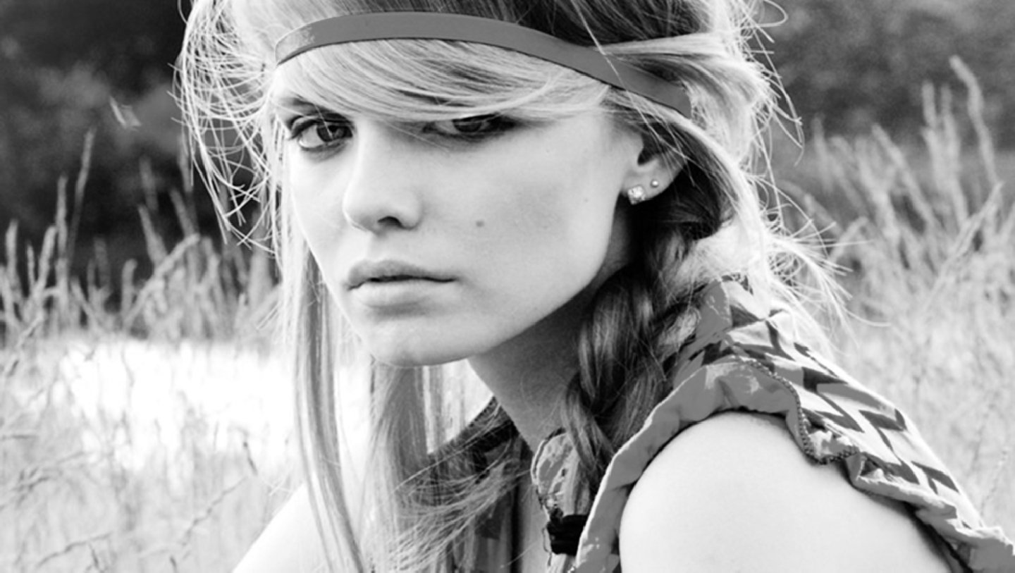Black-and-white portrait evoking the movie Life Is Beautiful: a pensive young woman with braided hair and a headband sits in a grassy field.
