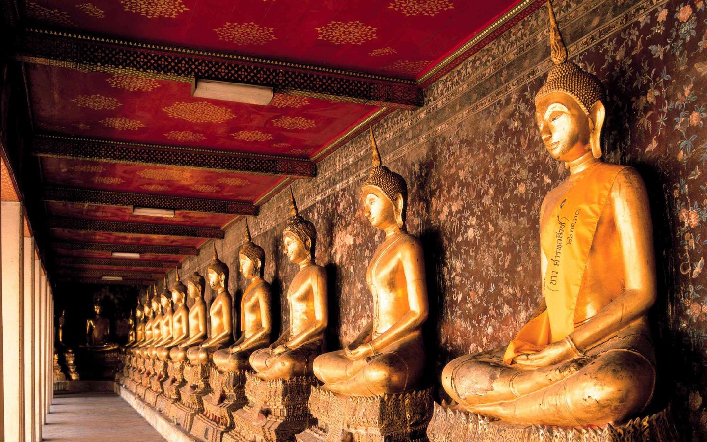 A serene corridor lined with golden Buddha statues, reflecting the beauty and tranquility of Buddhism within an ornate temple setting.