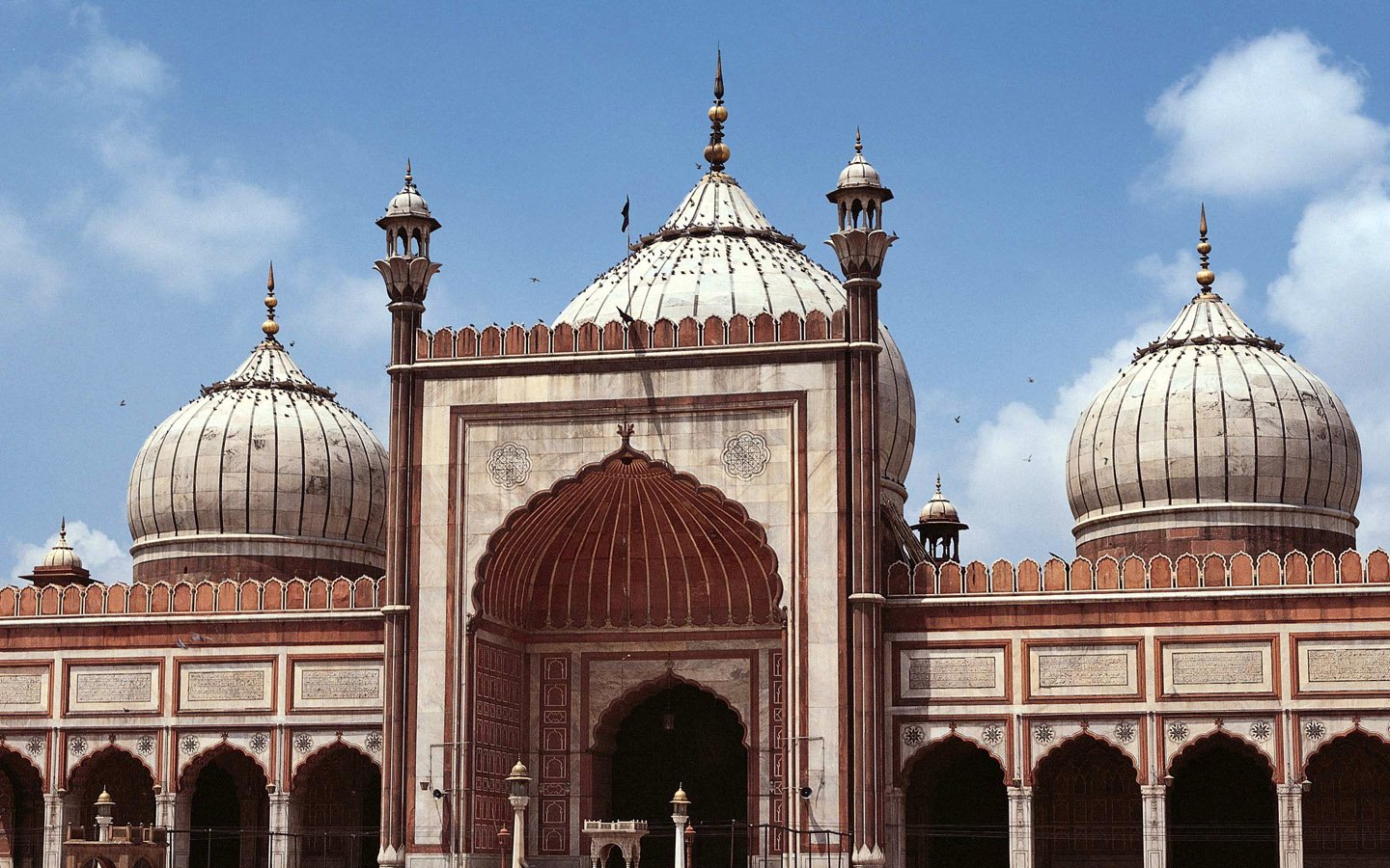A view of the majestic Jama Masjid in Delhi, showcasing its stunning domes and intricate architecture against a bright blue sky.