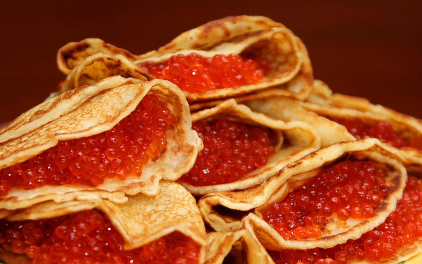 Folded blini filled with glossy red caviar piled on a warm wooden surface.
