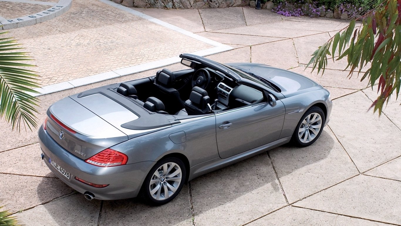 A silver BMW 650i convertible parked on a stone driveway with the top down, showing its sleek design and luxurious interior.