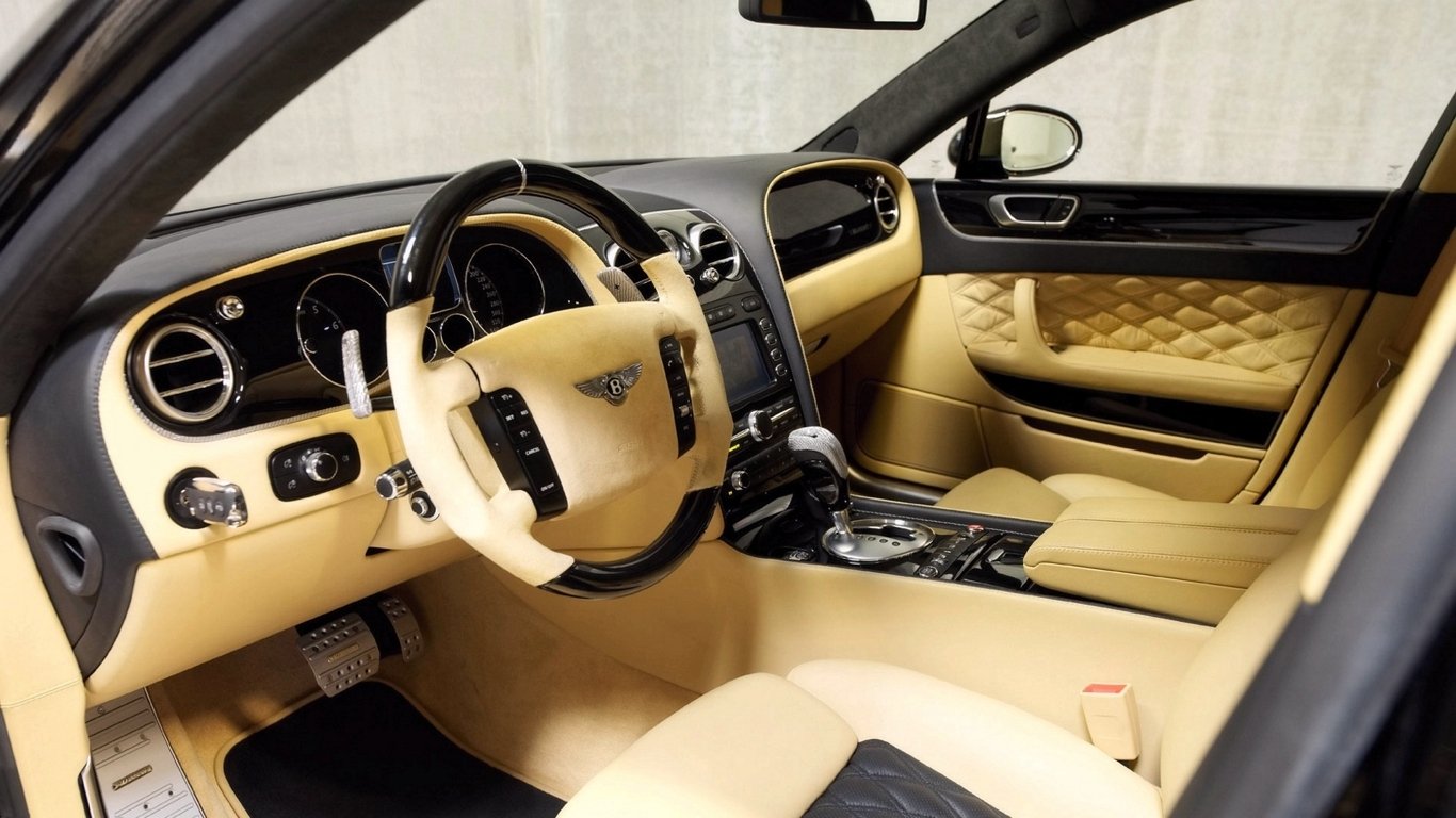 The interior of a Bentley Flying Spur features luxurious beige leather seats, a stylish dashboard, and elegant detailing, showcasing the vehicle's high-end craftsmanship.