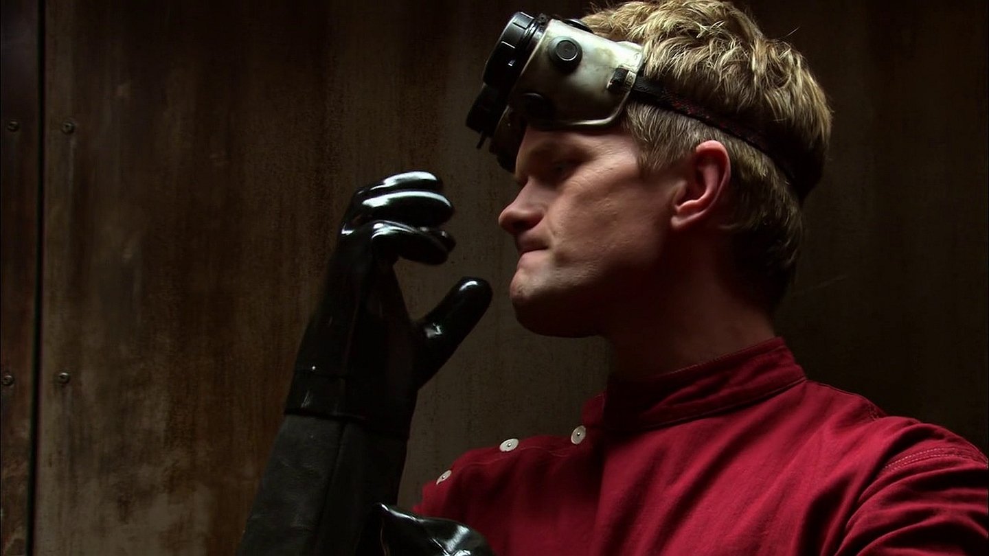 Side profile of a stern man in a red military-style coat and goggles, sliding on a black glove — a dramatic moment from the TV show Doctor Horrible's Sing-Along Blog.