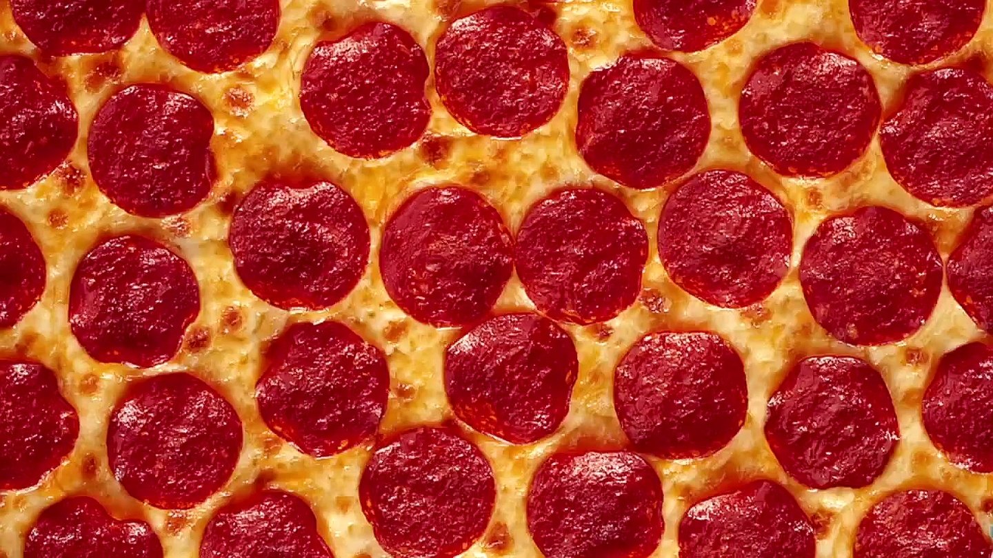 A close-up view of a pizza topped with abundant pepperoni slices arranged evenly over a golden, melted cheese base.