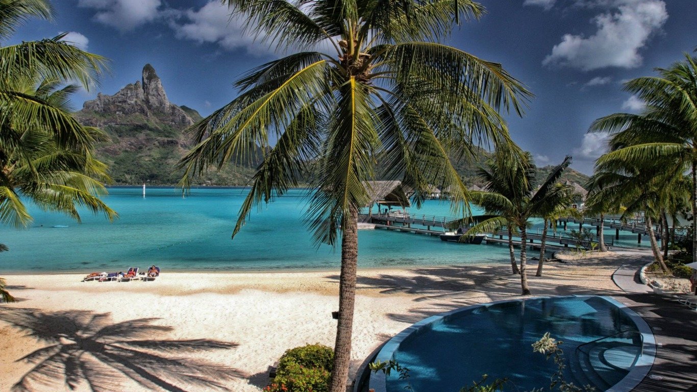 Tropical Maldives beach holiday scene: palm trees, white sand, turquoise lagoon, overwater bungalows and lounge chairs captured in bright travel photography.