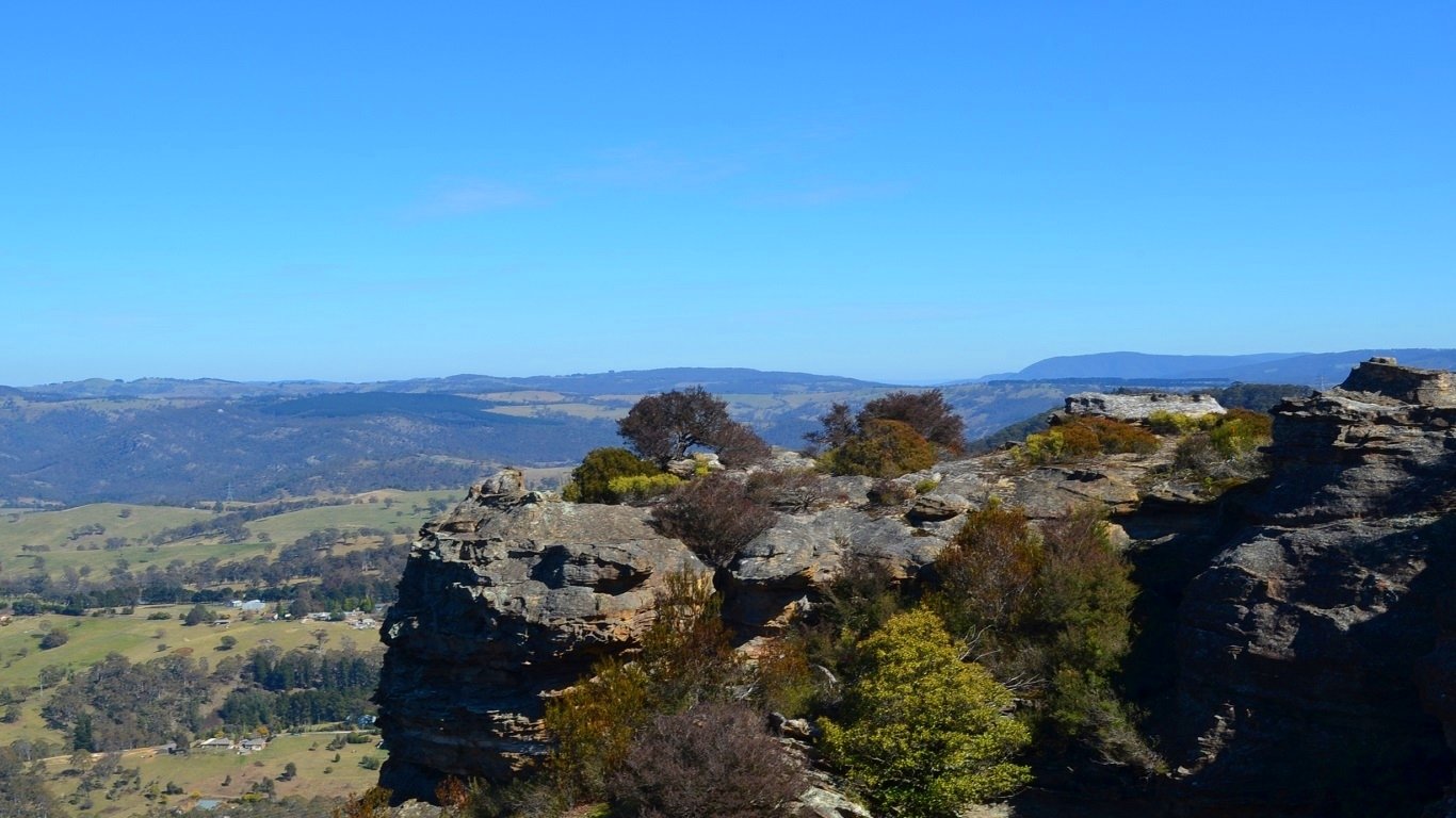 View from Hassans Walls Lookout, Blue Mountains, Australia: rugged cliff edge overlooking layered mountain ranges and valleys under a clear blue sky.