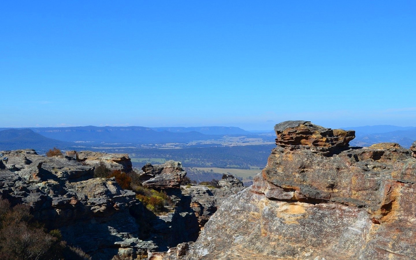 Rock formations at Hassans Walls Lookout with expansive views of the Blue Mountains landscape in Australia under a clear blue sky.