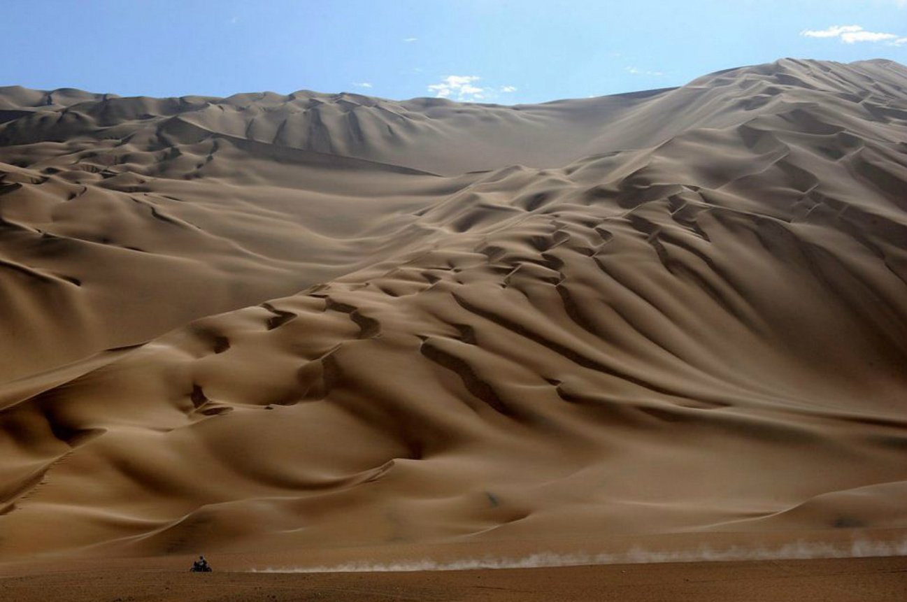 Vast desert landscape with rolling sand dunes under a clear blue sky, showcasing the natural texture and patterns formed by the wind.