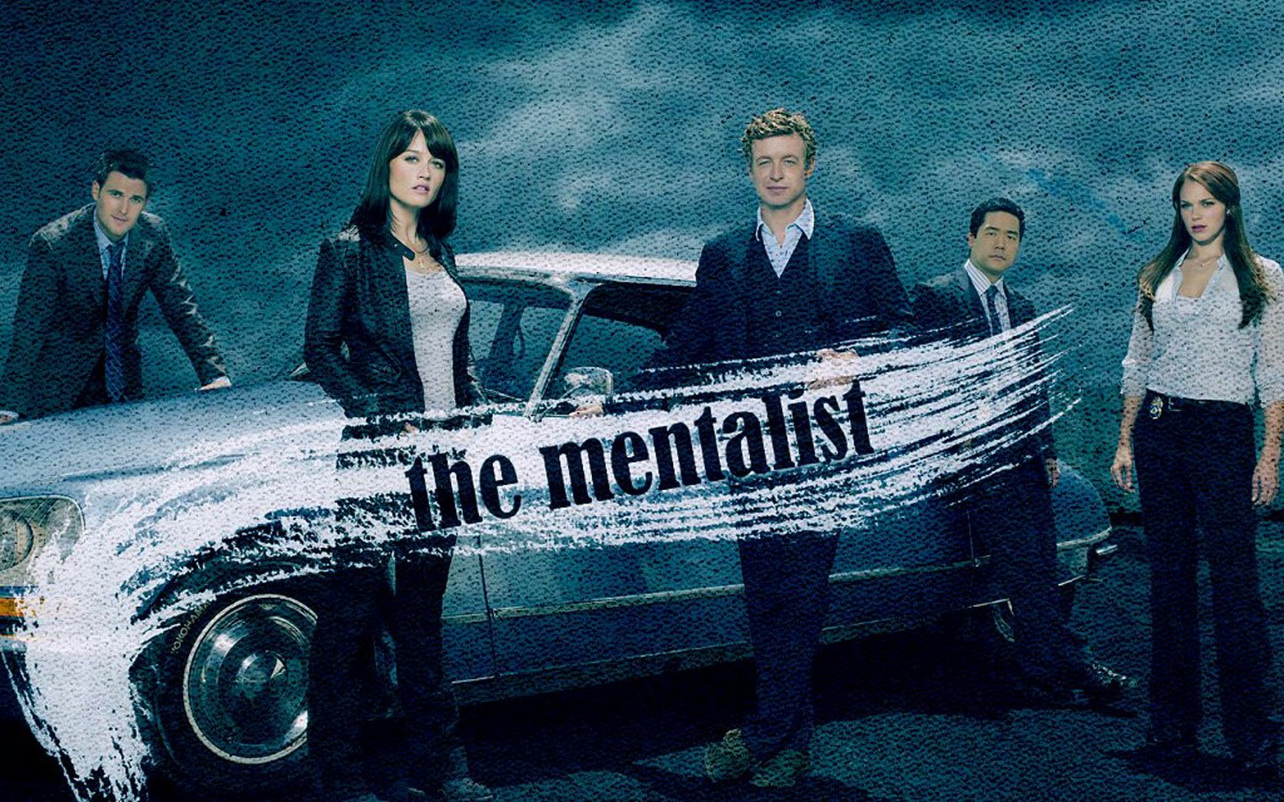 Cast members of the TV show The Mentalist stand around a vintage car under a moody sky, with the show's title prominently displayed across the vehicle.