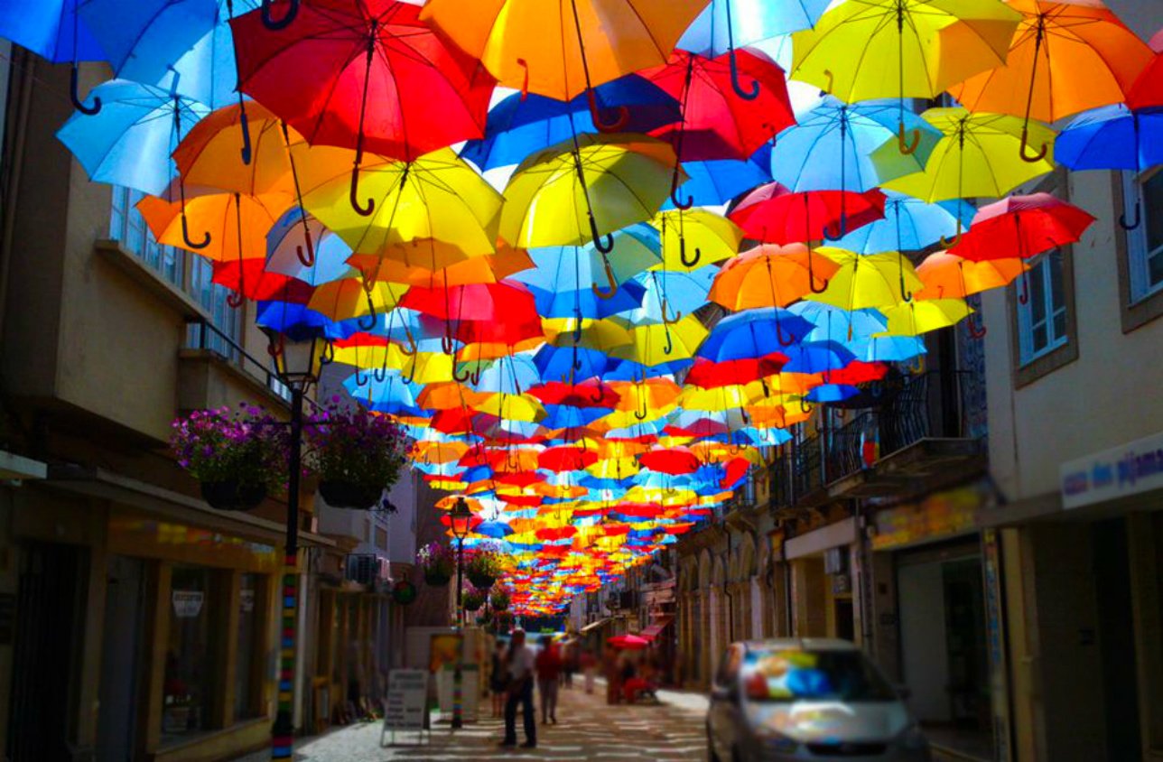 A vibrant street scene features an array of colorful umbrellas suspended overhead, creating a cheerful atmosphere and enhancing the charm of the photography.