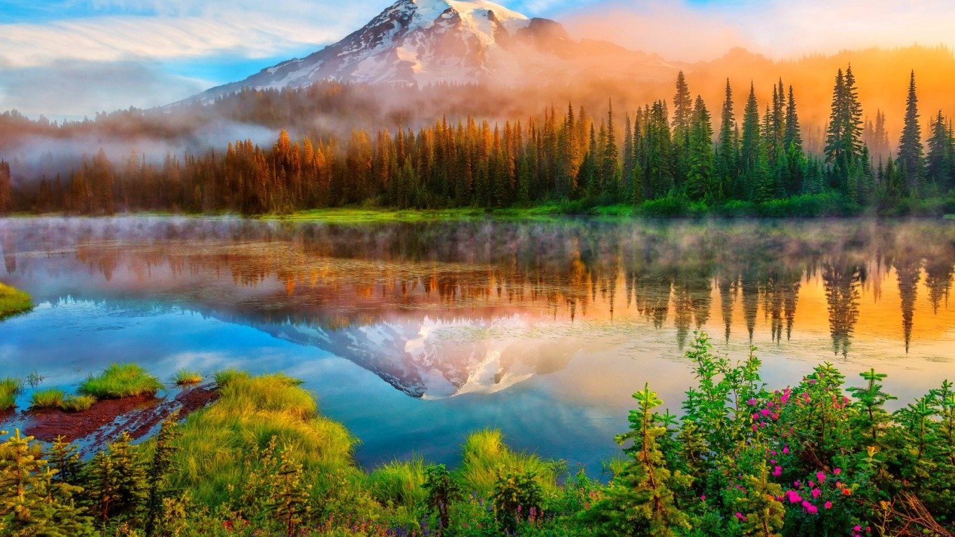 A serene lake captures the reflection of a majestic mountain, surrounded by lush greenery and mist, showcasing the beauty of nature at dawn.