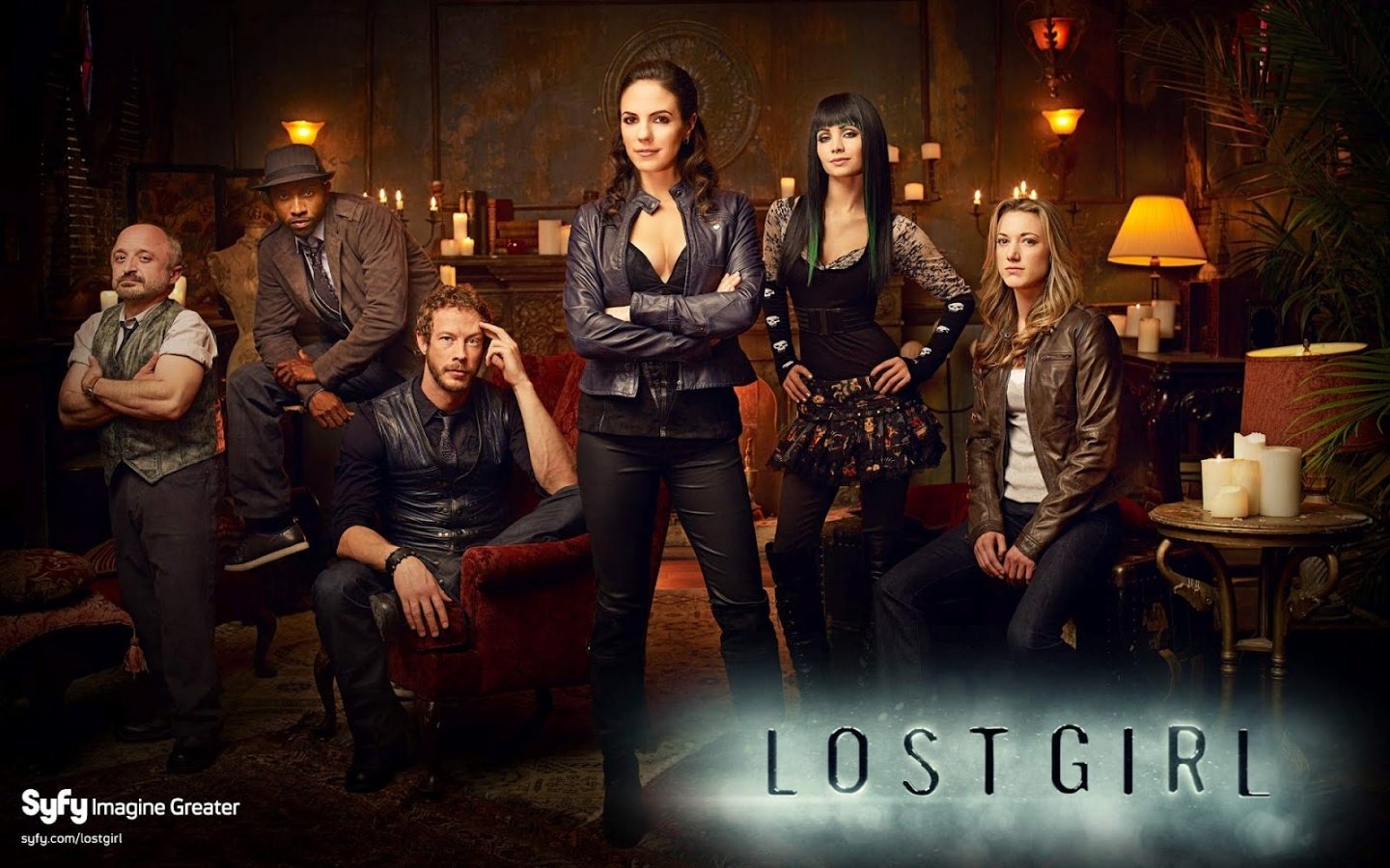 A group of main characters from the TV show Lost Girl stands confidently in a dimly lit room, surrounded by candles, each showcasing their distinct style and demeanor.