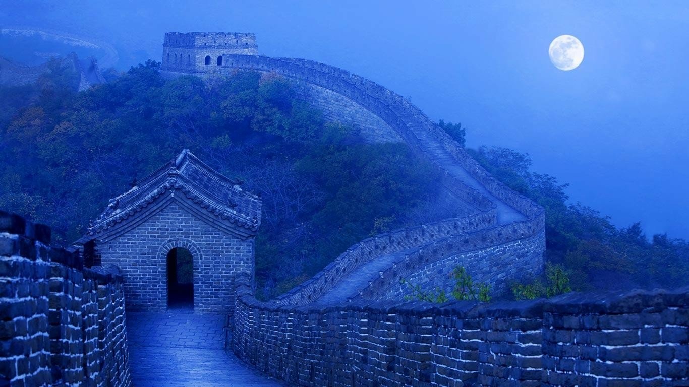 The man-made Great Wall of China stretches across misty hills beneath a glowing full moon in this serene nighttime landscape.