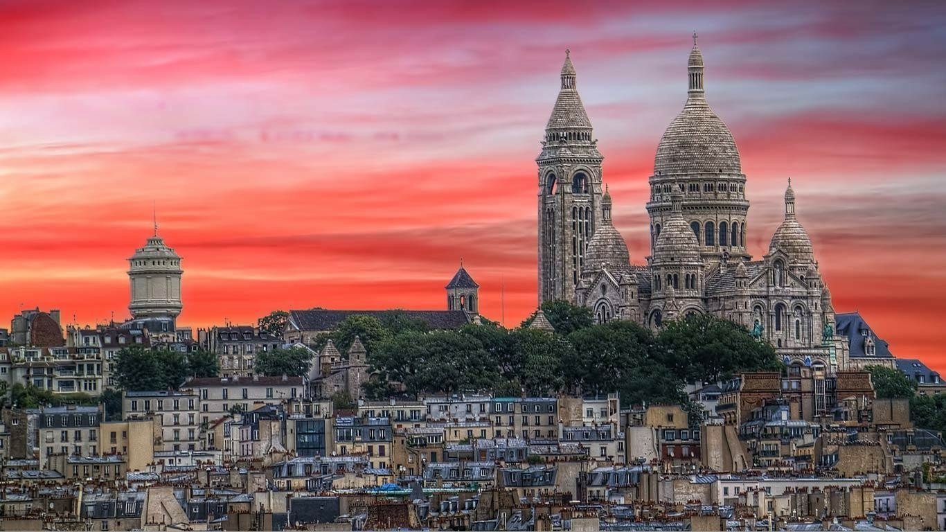A stunning view of Montmartre in Paris, France, showcasing the iconic Basilica of Sacré-Cœur against a vibrant sunset, overlooking the charming cityscape below.