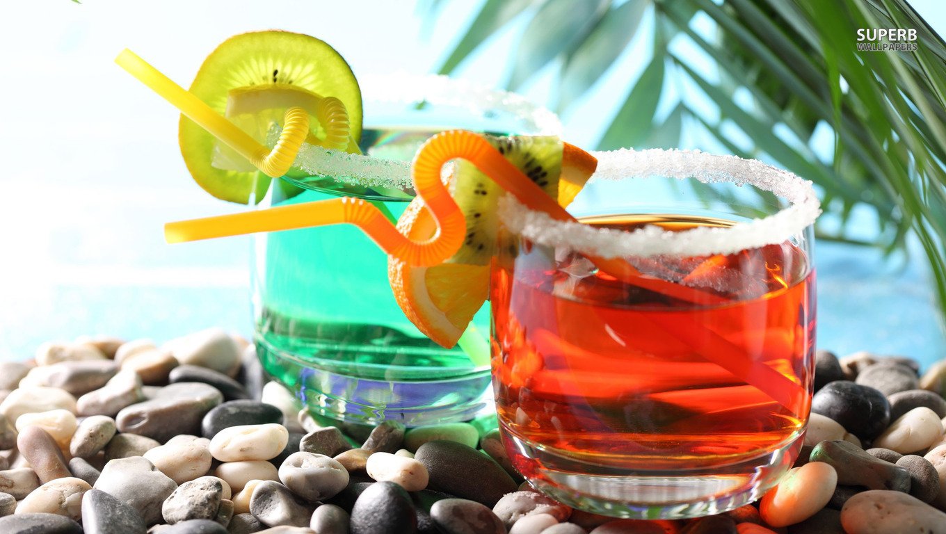 A vibrant display of two colorful cocktails on a bed of smooth stones, garnished with fresh fruit and playful straws, surrounded by tropical greenery.