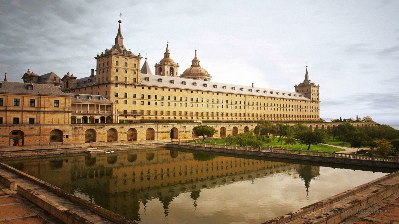 The image shows the man-made historic El Escorial palace and monastery with its reflection in the still water of a large rectangular pool.