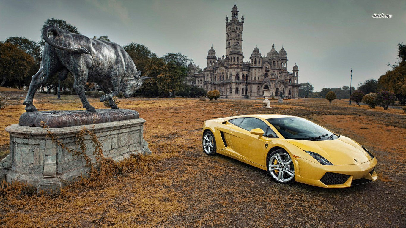 A yellow Lamborghini Gallardo is parked beside a majestic statue of a bull, set against a grand, historic building amid an empty landscape.