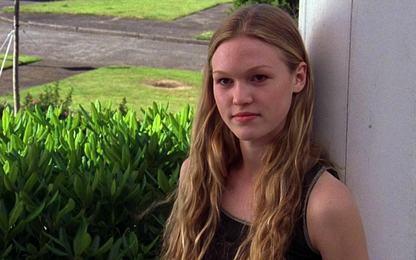 A young Julia Stiles leans against a pillar, surrounded by lush greenery, capturing a moment of contemplation and natural beauty.