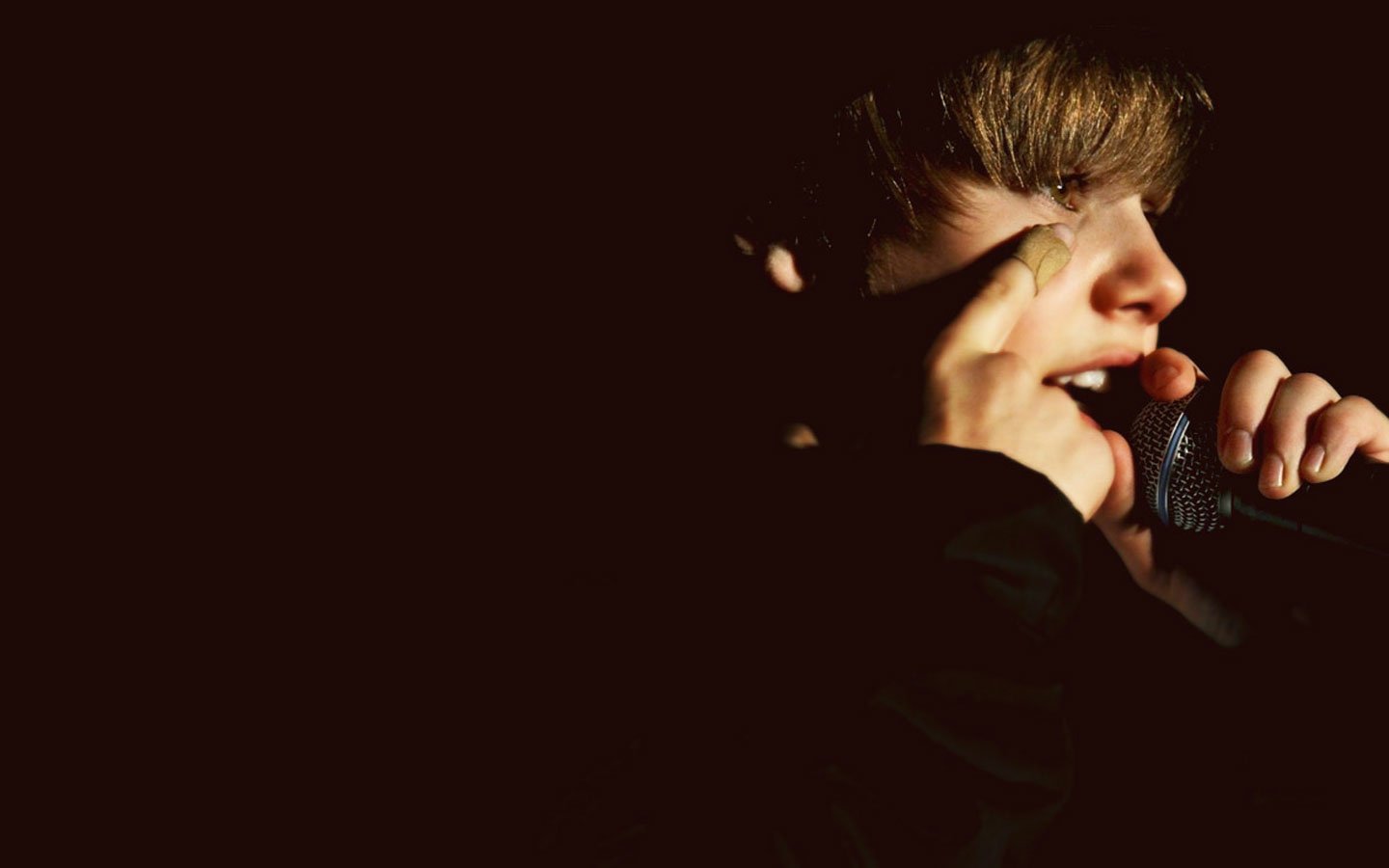 A close-up of Justin Bieber passionately singing into a microphone, illuminated by dramatic lighting, capturing the essence of his music performance.