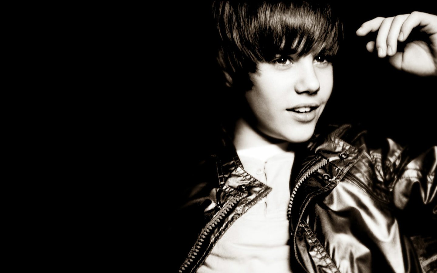 A black and white portrait of Justin Bieber, featuring him with a playful expression, wearing a shiny jacket and styled hair, embodying the spirit of music.