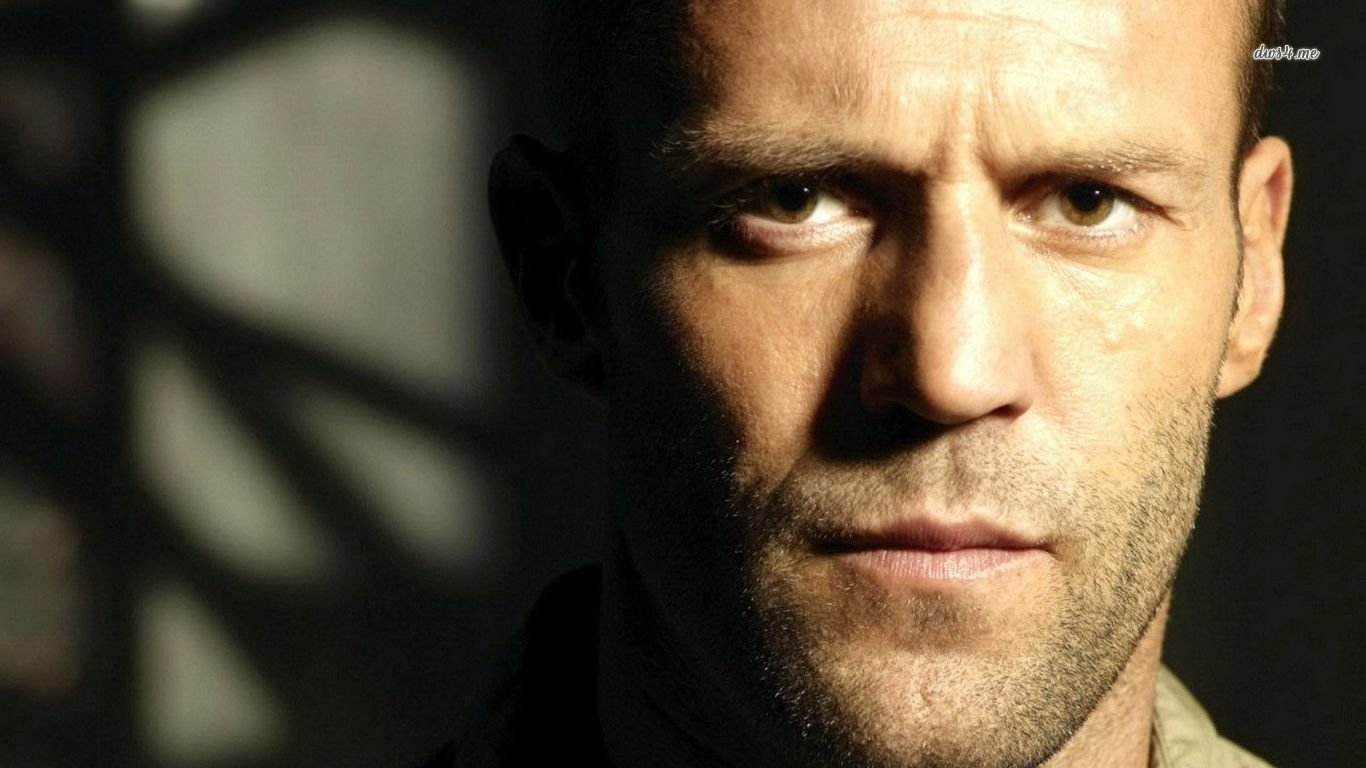 Close-up portrait of celebrity Jason Statham, showcasing his intense expression and rugged features against a shadowy background.