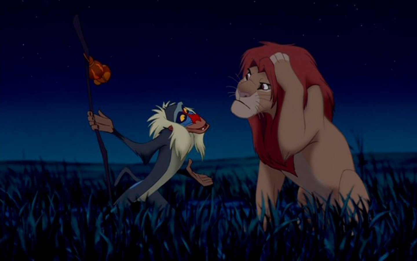 Scene from The Lion King (1994) featuring Rafiki holding a glowing staff, talking to Simba at night in the grasslands under a dark blue sky.