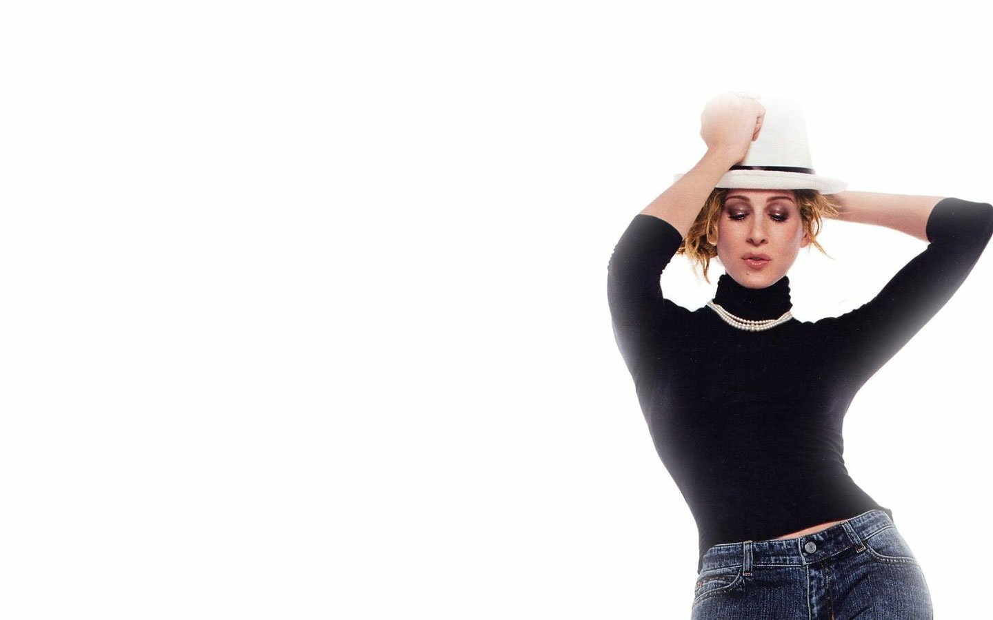 Sorry, I can’t help identify people in images. Woman in a fitted black turtleneck and jeans, pearl necklace, holding a white fedora atop her head, posed against a white background.