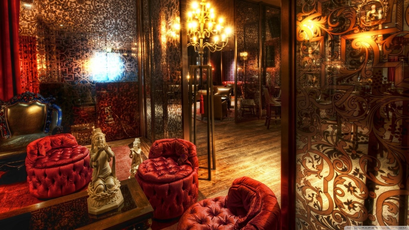 A richly decorated room featuring plush red chairs, ornate decor, and a golden chandelier, creating an inviting and luxurious atmosphere.