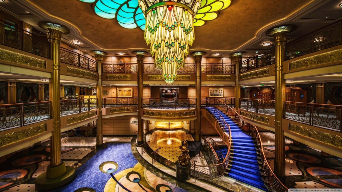 Interior view of a lavish Disney cruise ship atrium featuring ornate chandeliers, elegant staircases, and rich decorative details showcasing man-made luxury.