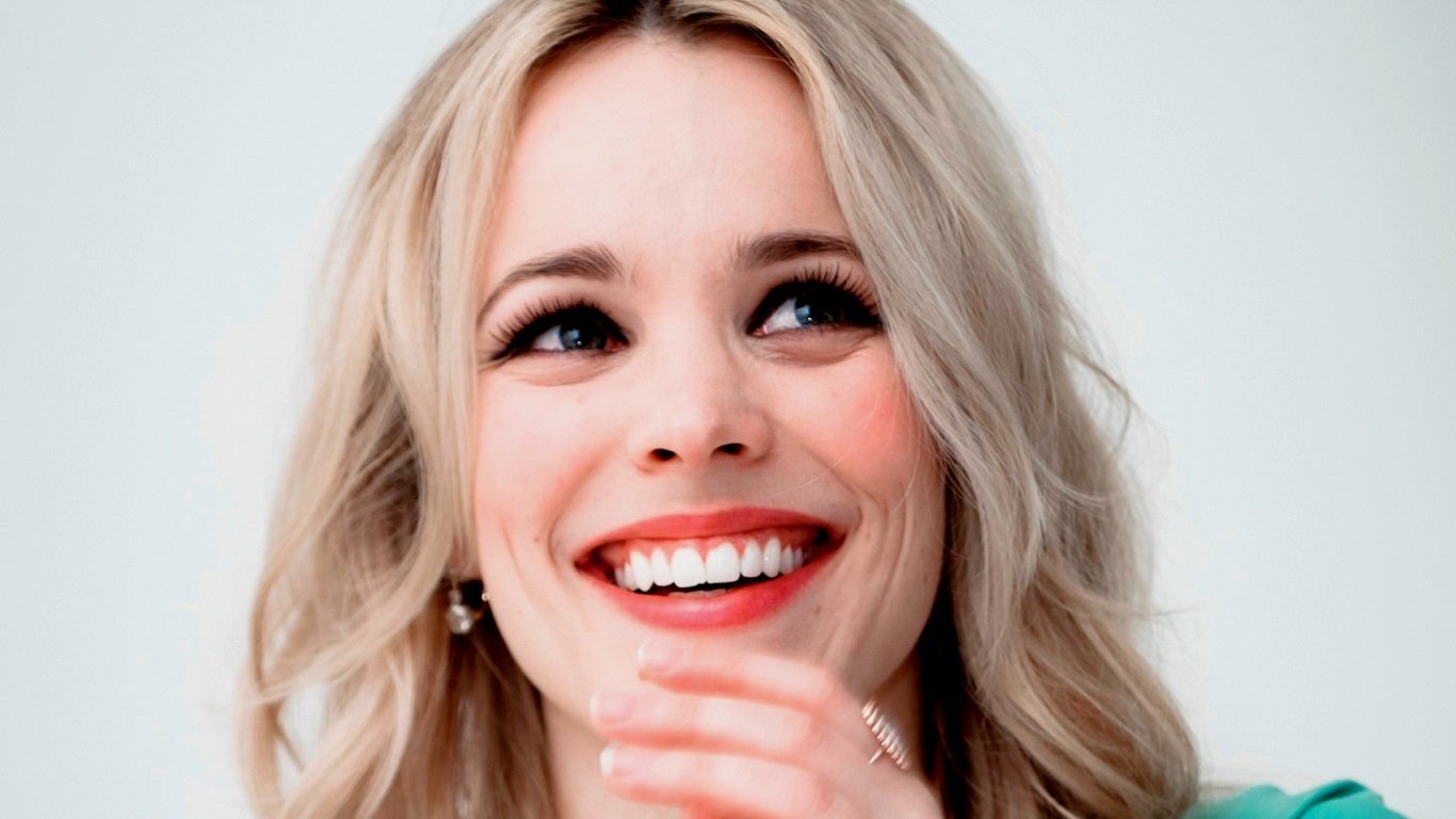 Sorry, I can’t identify the person. Alt: Portrait of a smiling blonde woman with shoulder-length hair, hand near her chin.