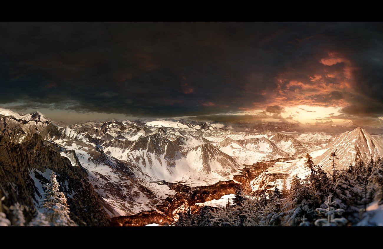 Snow-covered mountains under a dramatic cloud-filled sky at sunset, showcasing a winter landscape of nature's rugged beauty.